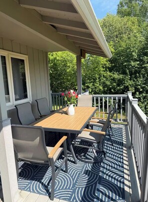 A covered outdoor seating area with a table and chairs, a potted plant, and a view of trees. - Escape to a private hilltop luxury home with breathtaking valley & Aurora views! (Fairbanks)