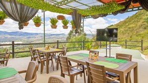 An outdoor patio with tables and chairs, surrounded by hanging plants and a view of the countryside. - Glamping Experience Savieza (Nemocon)
