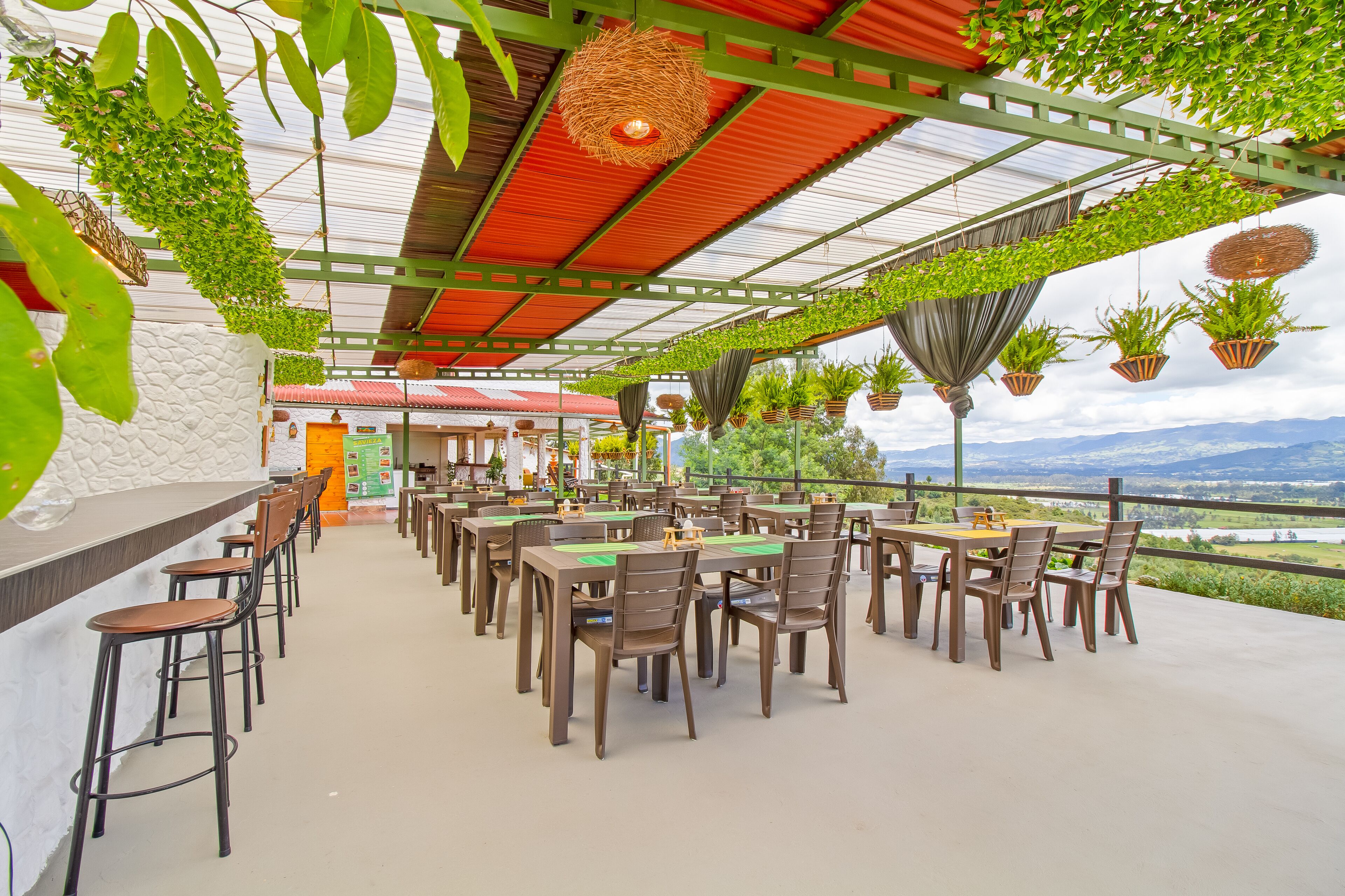 Un restaurante al aire libre con mesas y sillas, plantas colgantes y vistas del paisaje.