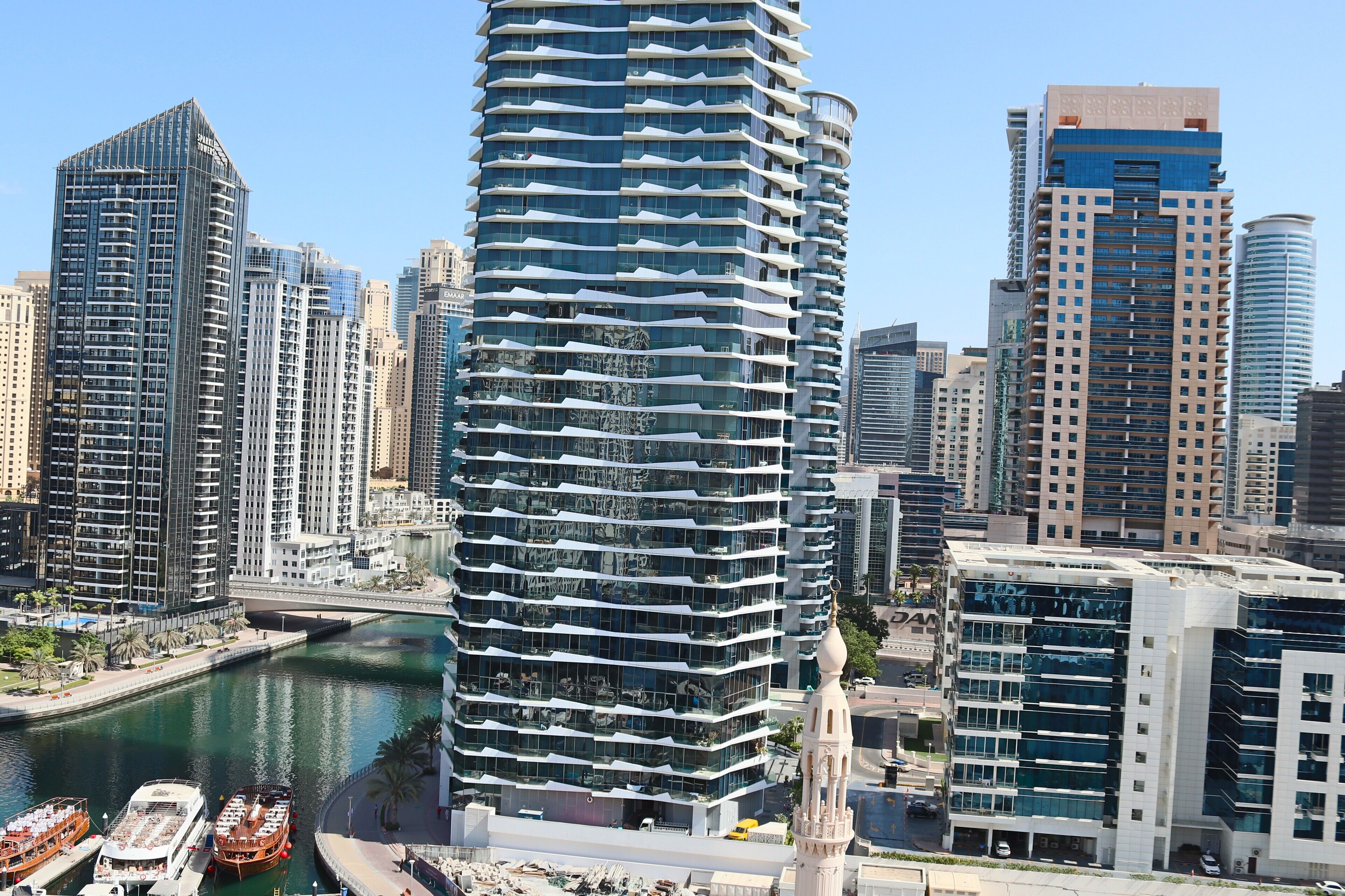 Un hôtel moderne de grande hauteur, doté d’une façade incurvée originale, situé près d’une promenade en bord de mer où sont amarrés des bateaux.