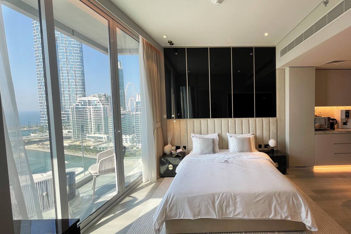 Ein modernes Hotelzimmer mit einem großen Bett, Blick auf eine Stadtlandschaft und einem Balkon.