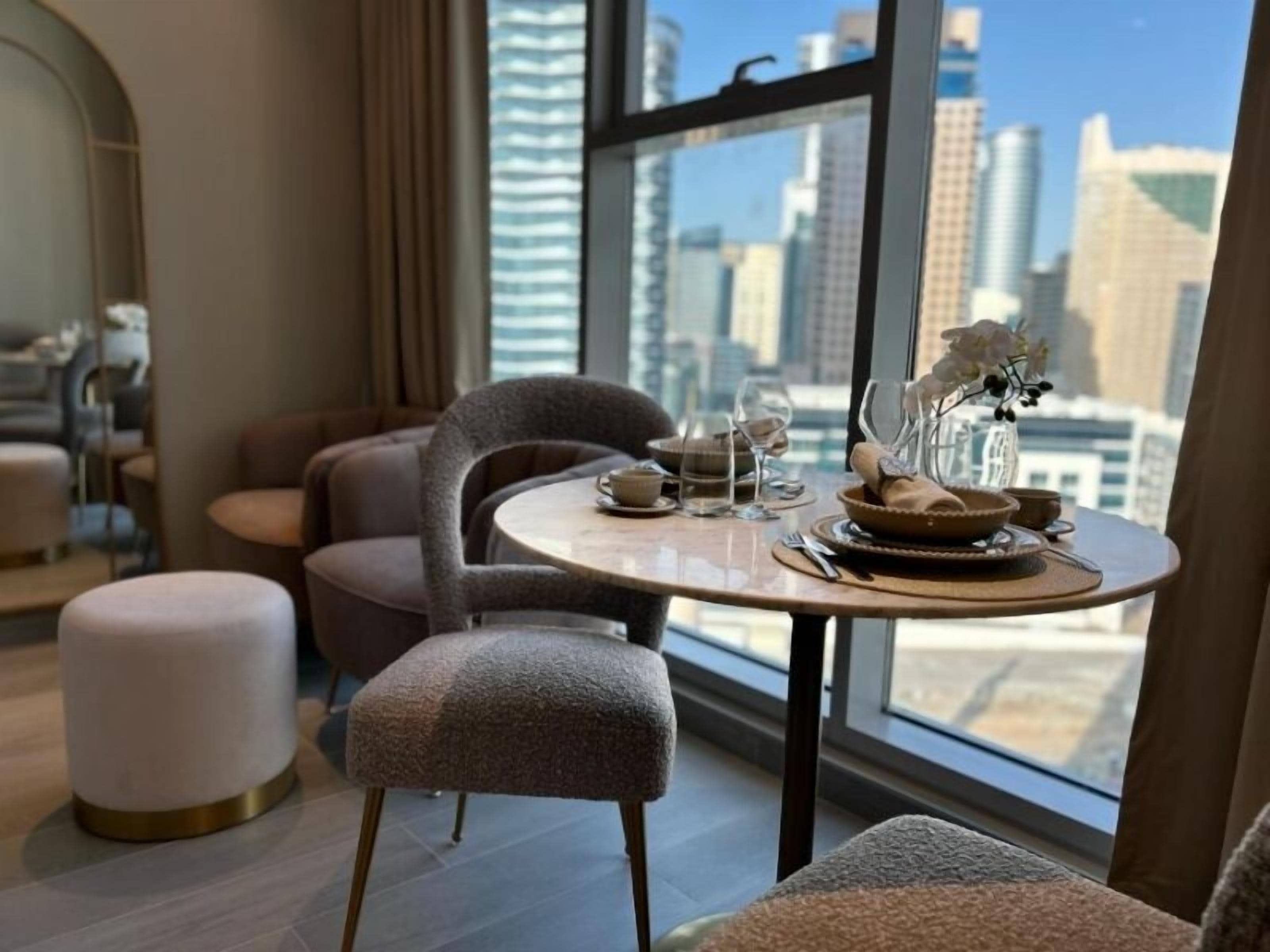 Un comedor con una mesa redonda, sillas tapizadas en gris y vistas a la ciudad a través de amplias ventanas.