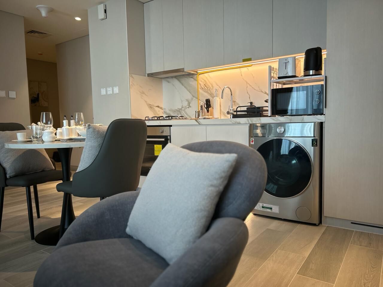 Una cucina moderna con lavatrice integrata, zona pranzo con sedie rivestite in grigio e pannello di marmo a rivestimento.