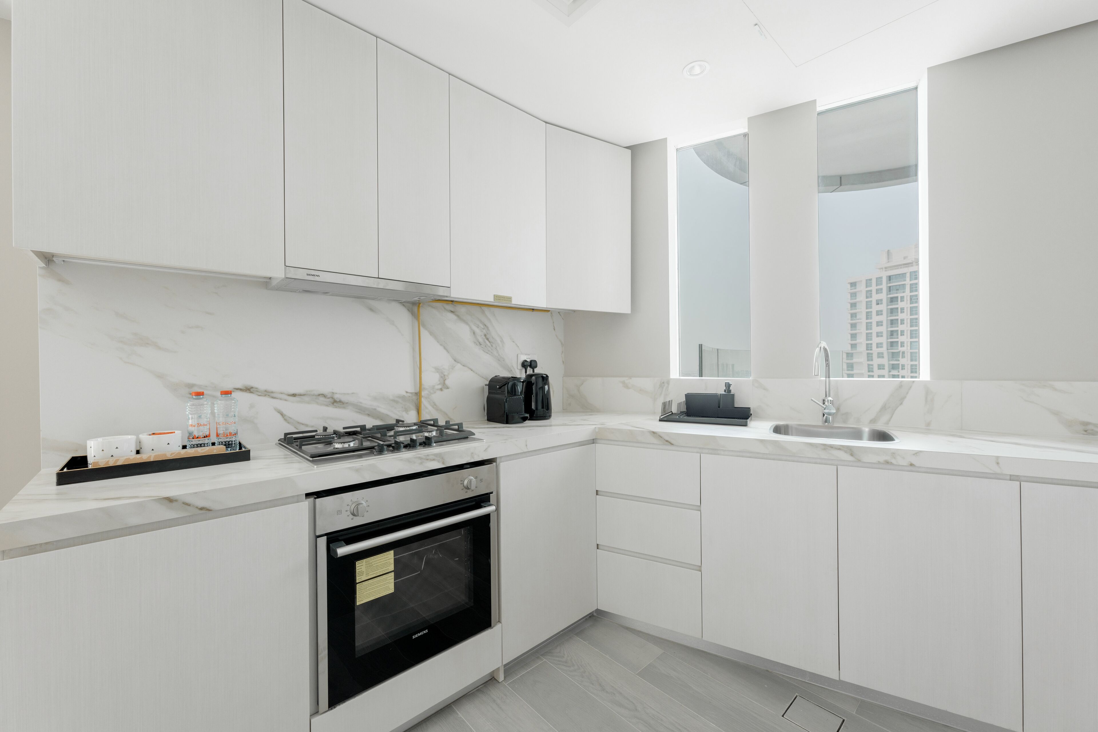 A modern kitchen with white cabinets, a marble countertop, a built-in oven, and a window with a city view.