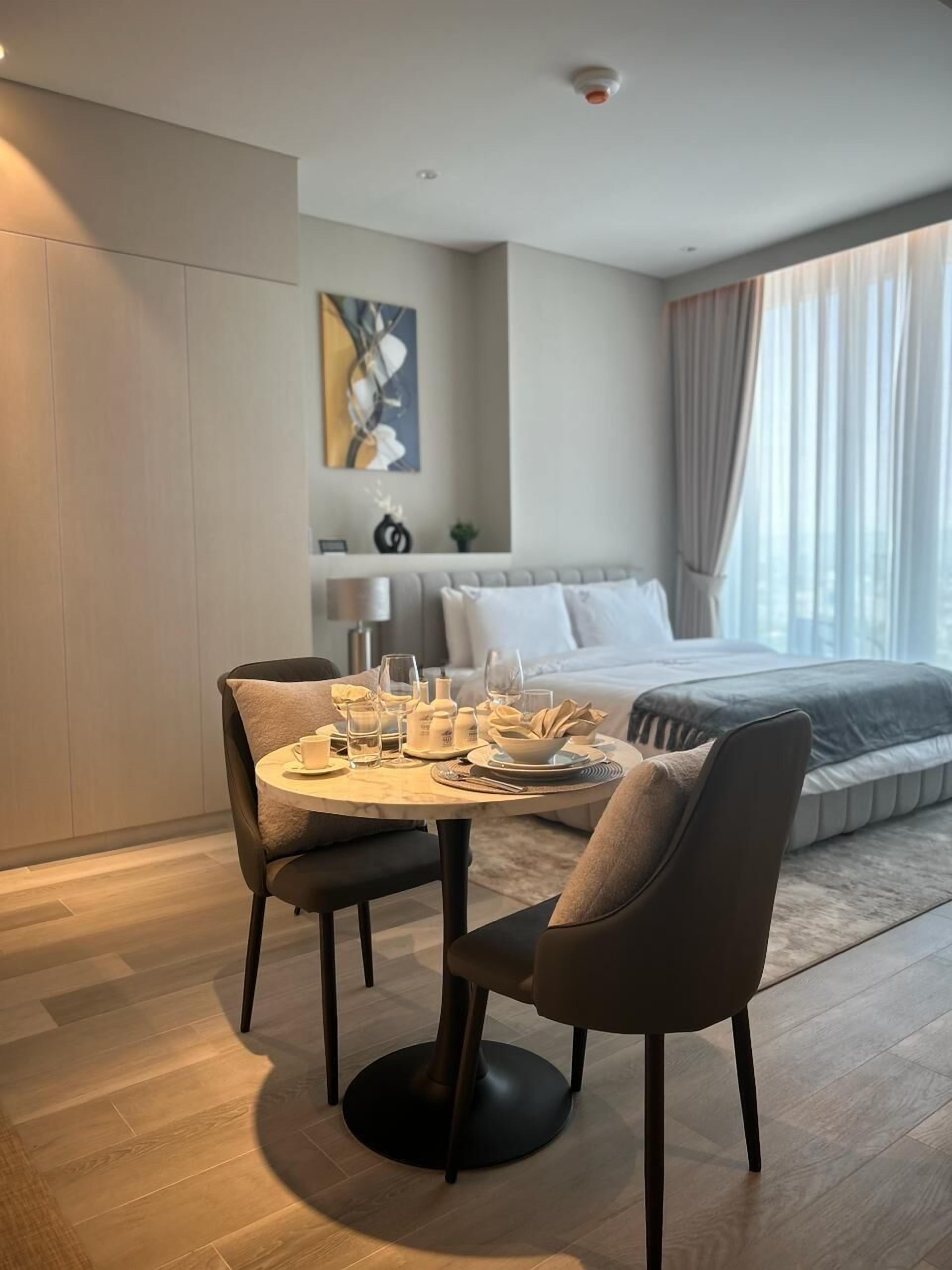A modern hotel room with a dining area, a bed, and a large window with curtains.