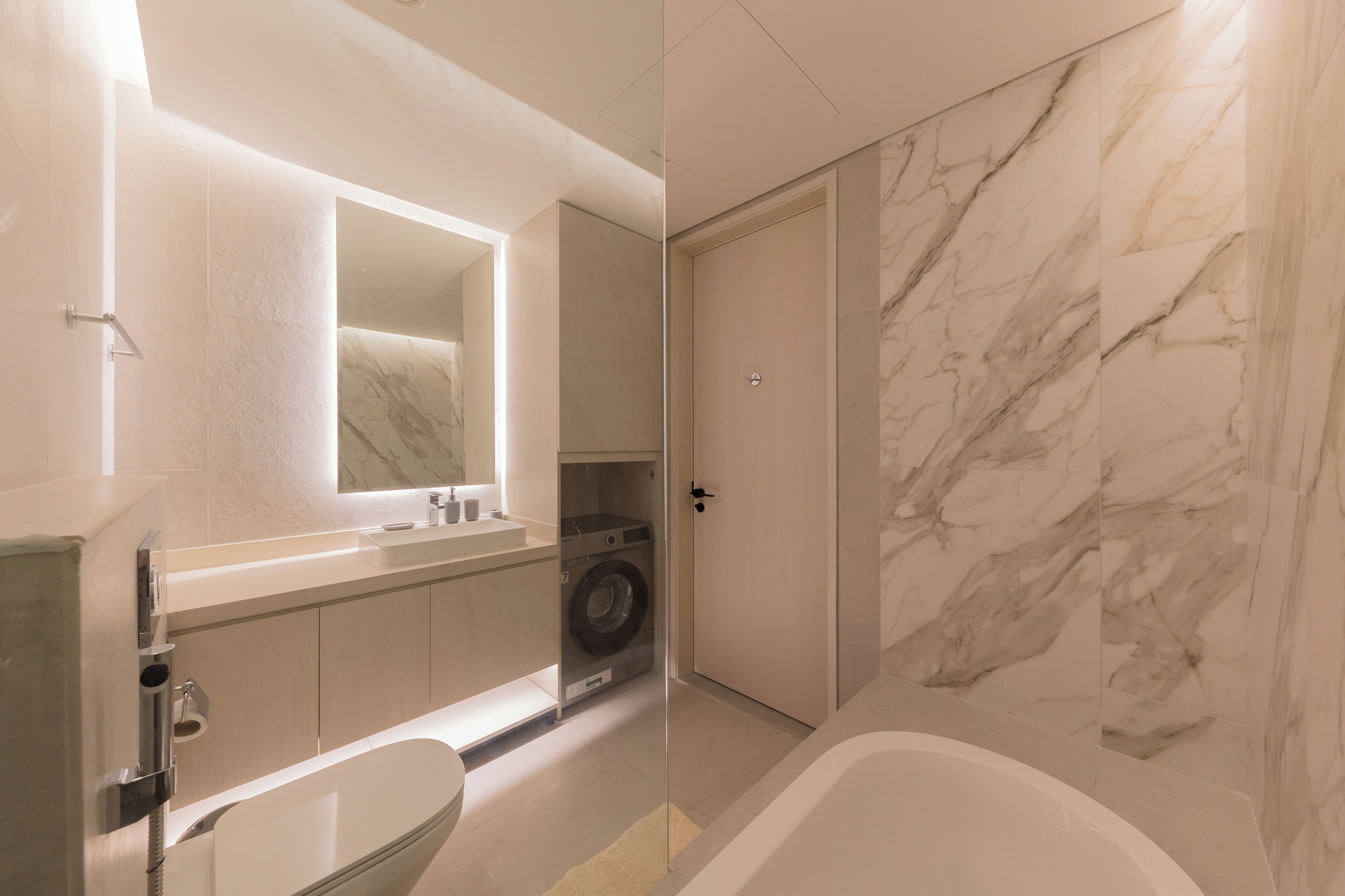 Un baño moderno con pared de mármol, lavadora integrada, bañera y un espejo grande.