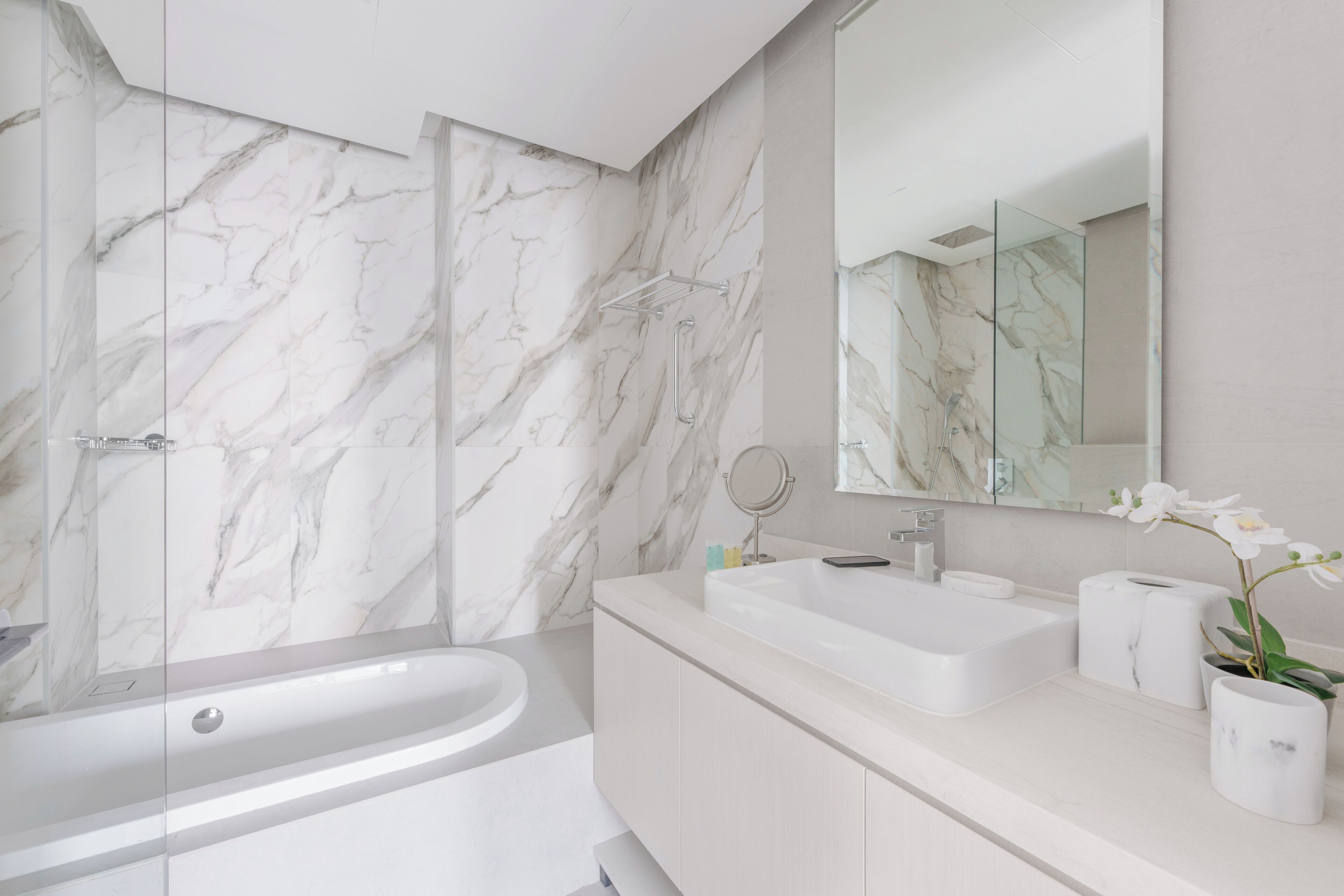 A modern bathroom with a marble wall, a bathtub, a sink, and a mirror.