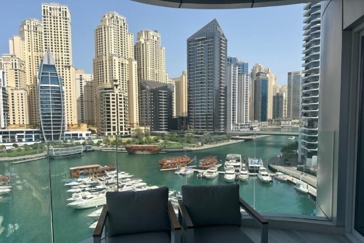 Ein Balkon mit zwei Stühlen mit Blick auf einen Hafen voller Boote und hoch aufragende Gebäude im Hintergrund.