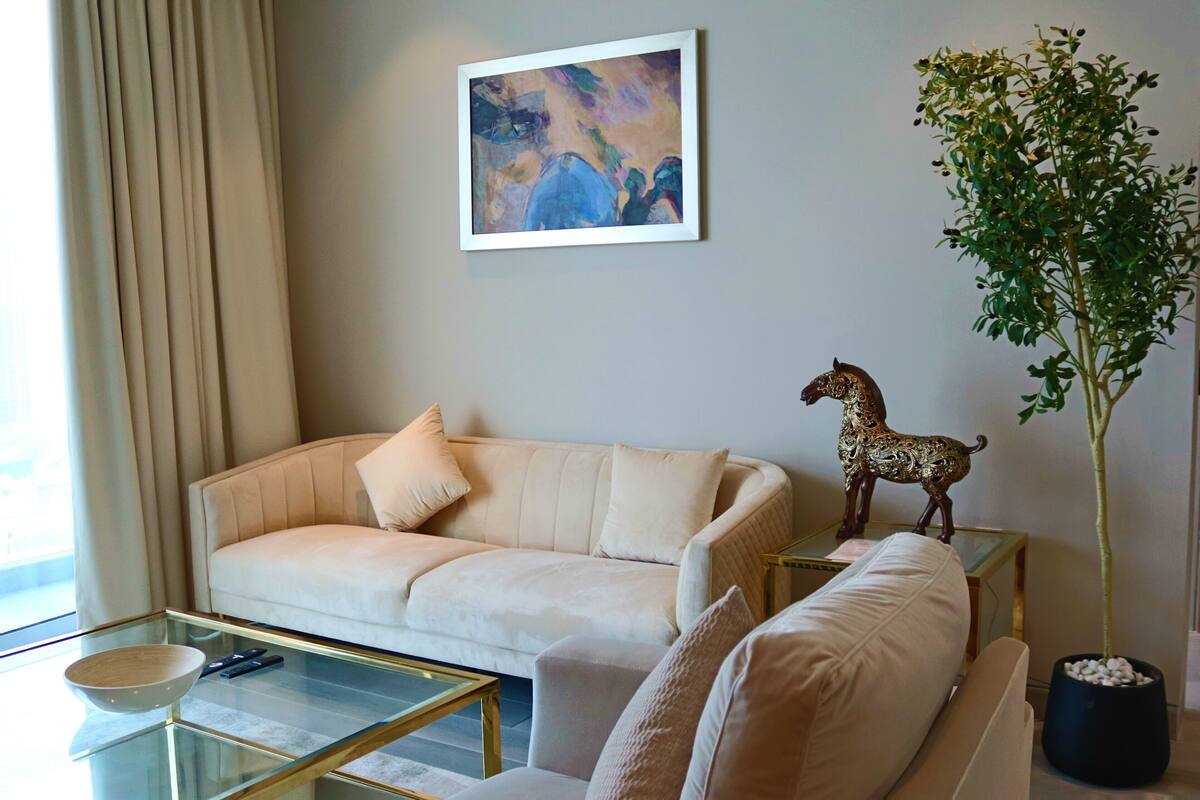 Ein Wohnzimmer mit einem beigefarbenen Sofa, einem Glastisch, einem gerahmten abstrakten Gemälde, einem Blumentopf und einer dekorativen Pferdefigur.
