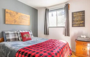 Cozy retreat with a neatly made bed, wooden headboard, and a large artwork above.