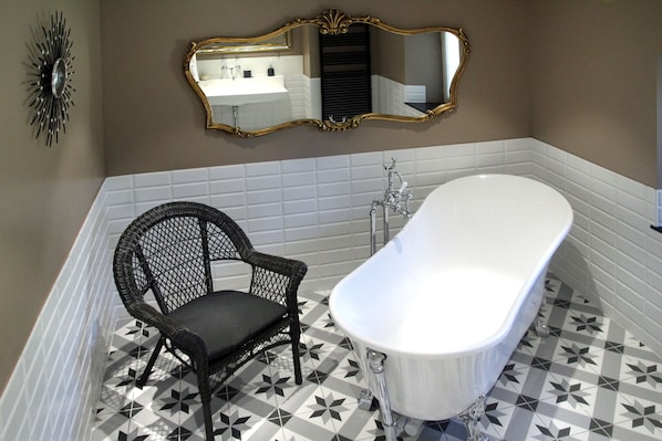 A bathroom with a freestanding bathtub, a chair, and a mirror with an ornate frame.