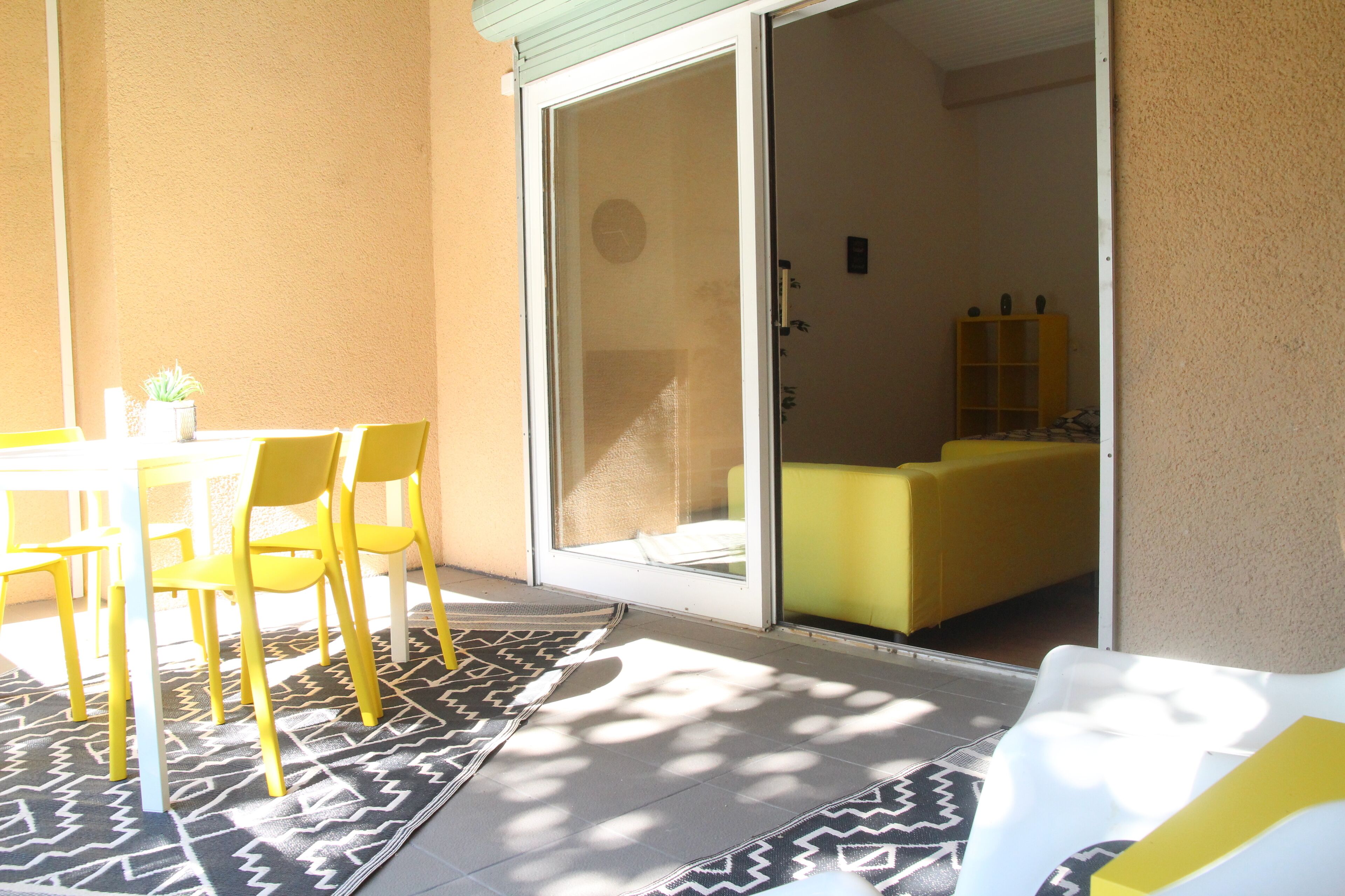 A patio area with a table and chairs, a sliding glass door leading to an interior room, and a patterned rug.