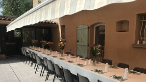 Un área de comedor al aire libre con una mesa larga dispuesta para una comida, rodeada de sillas.