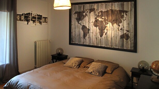 Une chambre avec un grand lit, une carte du monde accrochée au mur, un globe posé sur une table d’appoint et une lampe.