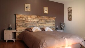 Un dormitorio con cabecera de madera, una cama con edredón color beige, dos mesitas de noche con lámparas y decoración en la pared.