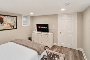 A bedroom with a bed, a dresser, a flat-screen TV, a door, and a painting on the wall.