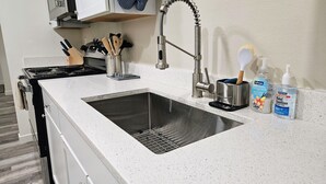 Une cuisine dotée d’un évier en acier inoxydable, d’un robinet moderne et d’un plan de travail muni d’un bloc à couteaux et d’un distributeur de gel hydroalcoolique.