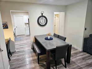 A dining area with a wooden table, benches, and a wall clock. - Stylish Cottage - Pets & Arcade - Minutes to Airport (North Charleston)