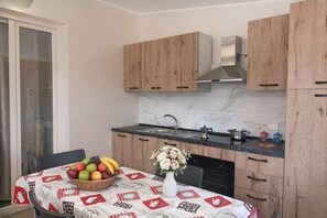 Une cuisine moderne avec des meubles en bois, un pare-feu en marbre et une table à manger agrémentée d’un panier de fruits et d’un vase de fleurs.