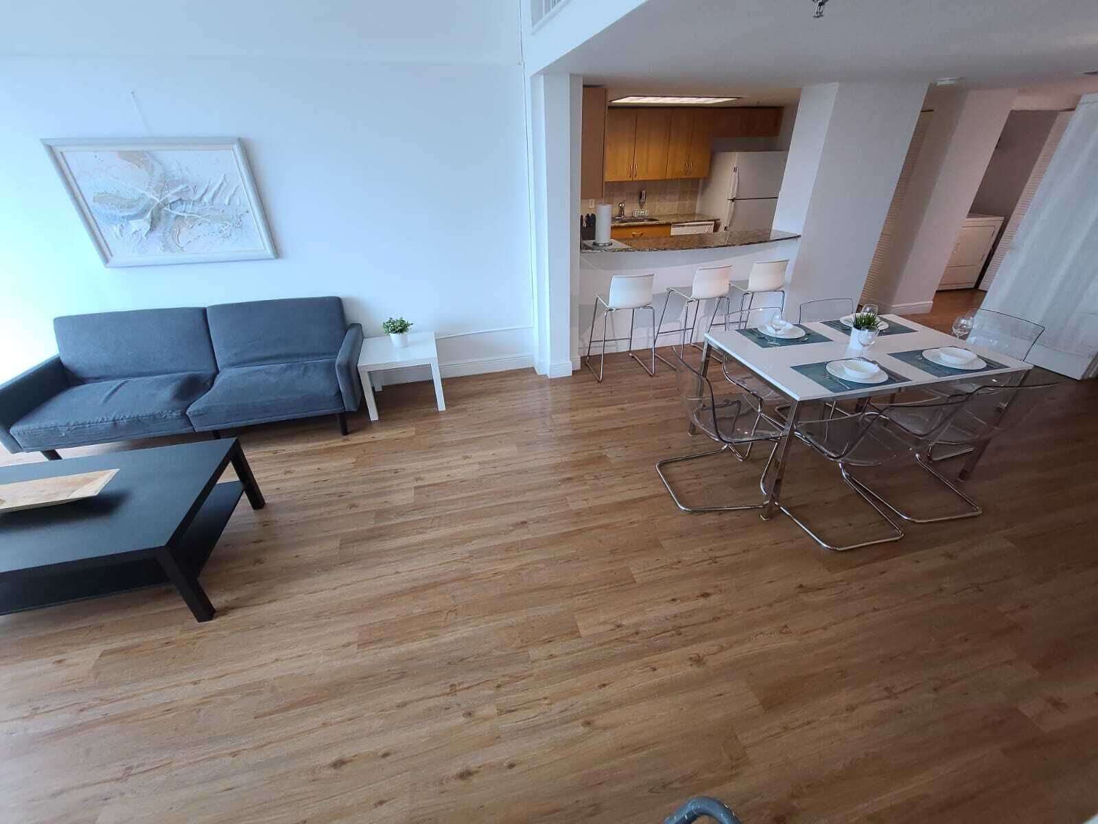 Un soggiorno moderno con un divano, un tavolo da pranzo con sedie e una cucina visibile sullo sfondo.