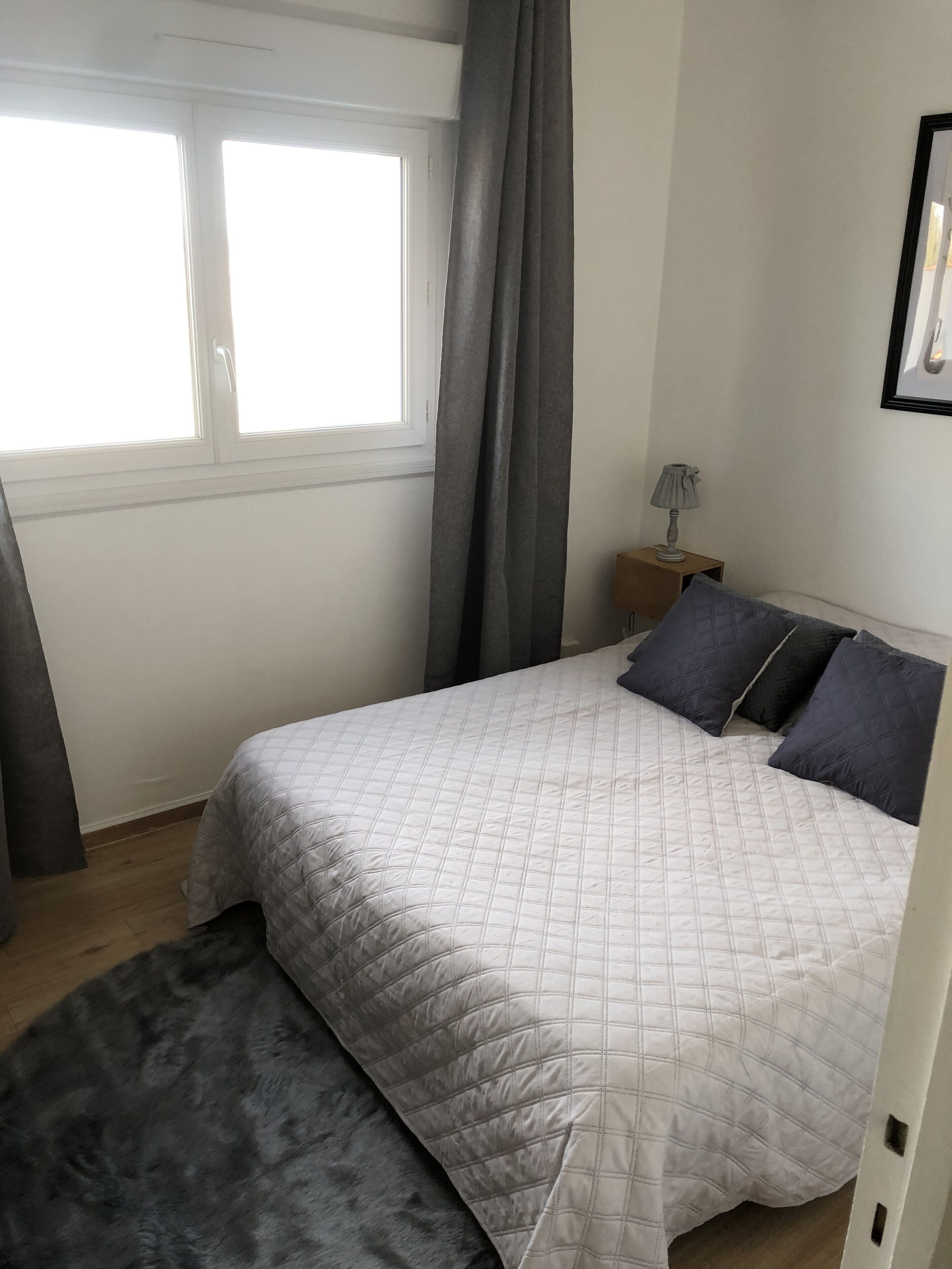 A bedroom with a bed, a nightstand, a lamp, and a window with curtains.