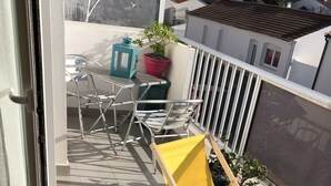 A balcony with a yellow chair, metal chairs, a potted plant, and a view of neighboring houses. - Lapart Challandais (Challans)