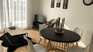 A modern living room with a round dining table, white chairs, a black coffee table, a TV, and artwork on the wall. - Lapart Challandais (Challans)