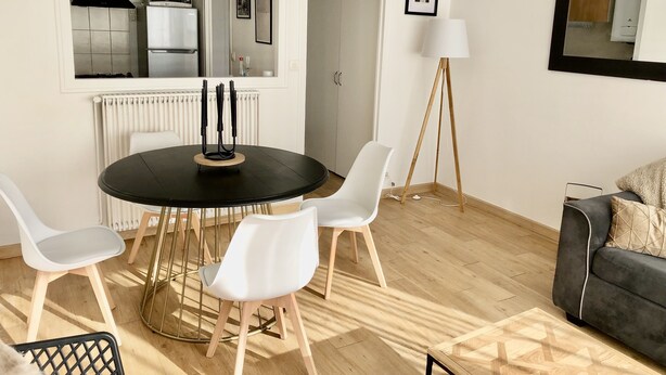 A modern living room with a round dining table, white chairs, a grey sofa, and a floor lamp. - Lapart Challandais (Challans)