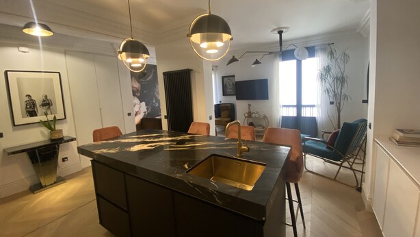 Een moderne keuken met een centraal eiland, hangende lampen en een eethoek met stoelen.