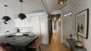 Een moderne keuken met witte kasten, een marmeren aanrechtblad en een centraal eiland met roze stoelen.