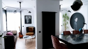 Een moderne woonkamer met een bank, een gitaar, een stoel en een eettafel met stoelen.