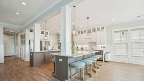 Una cocina moderna con una isla central, taburetes de bar, iluminación colgante y armarios blancos.