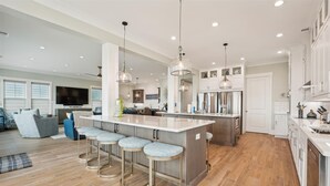 Una cocina moderna con una isla central, taburetes de bar, electrodomésticos de acero inoxidable y un amplio ventanal.