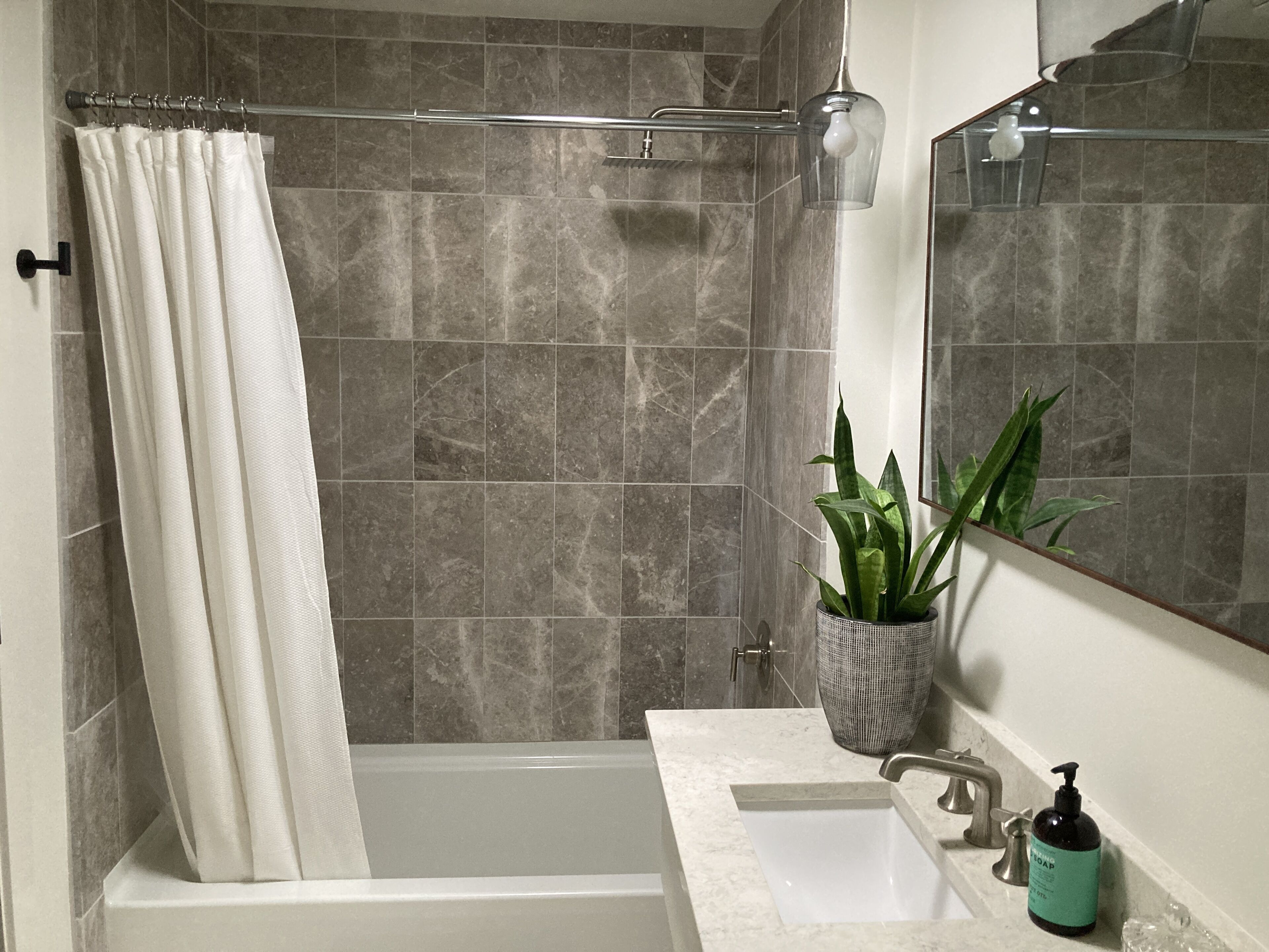 Ein modernes Badezimmer mit Badewanne, Waschbecken, Spiegel, Duschvorhang und einer Topfpflanze.