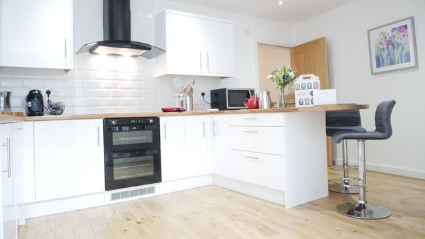 A modern kitchen with white cabinets, a black range hood, a microwave, and a coffee machine. - The Gill Penthouse (Ulverston)