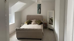 A bedroom with a large bed, a nightstand, a mirror, and a painting on the wall. - Lovely 2 Bedroom Loft Apartment in Buxton (Buxton)