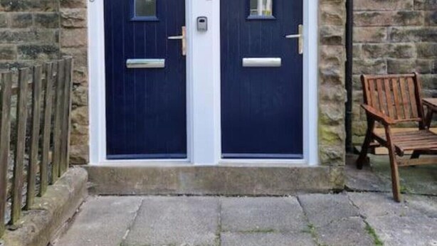 A double door entrance with a stone wall backdrop, numbered doors, and a wooden chair outside. - Lovely 2 Bedroom Loft Apartment in Buxton (Buxton)