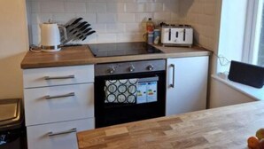 A compact kitchen with white cabinets, a wooden countertop, a built-in oven, and a window providing natural light. - Lovely 2 Bedroom Loft Apartment in Buxton (Buxton)