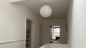 A narrow hallway with white walls and a white railing. A wooden ladder is visible in the background, leading to an upper level. - Lovely 2 Bedroom Loft Apartment in Buxton (Buxton)