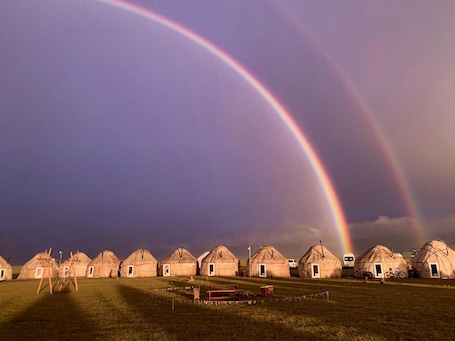 Yurts arranged in a row with a rainbow in the sky.