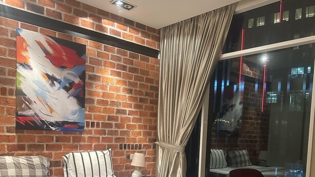 A modern hotel room with a brick accent wall, a large bed with white bedding, a desk, and a view of the city at night. - Soho Suites KLCC by Inam Suites (Kuala Lumpur)