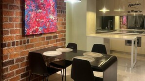 A modern kitchen with a brick wall, a colorful abstract painting, and a dining area with black chairs and a white table. - Soho Suites KLCC by Inam Suites (Kuala Lumpur)