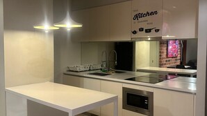 A modern kitchen with a white table, pendant lights, a stainless steel sink, and a sign that reads "This Kitchen is Seasoned with Love." - Soho Suites KLCC by Inam Suites (Kuala Lumpur)