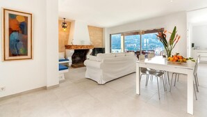 A modern living room with a white sofa, a dining table with chairs, a fireplace, and a large window offering a view of the city. - H2916 Holiday apartment Guillem in Cala San Vicente (Cala Sant Vicenç)