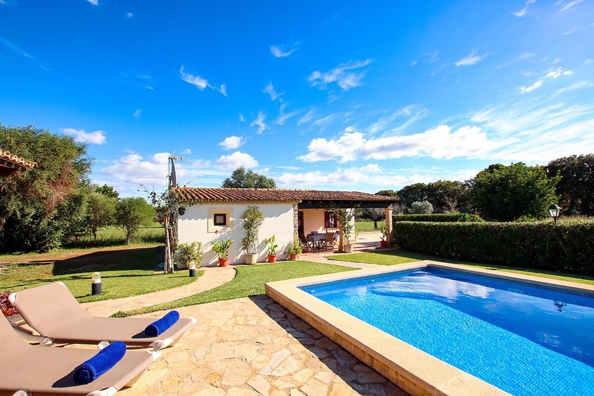 A swimming pool with lounge chairs, a small house, and a well-maintained garden.
