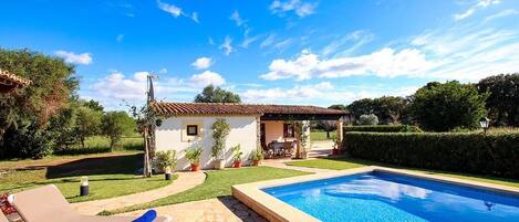 A swimming pool with lounge chairs, a small house, and a well-maintained garden.