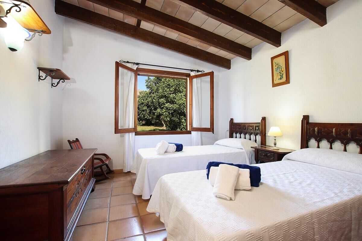 A hotel room with two beds, a wooden desk, a chair, a window with curtains, and a framed picture on the wall.