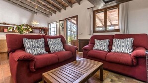 A living room with two red sofas, patterned cushions, a wooden coffee table, and a kitchen area in the background. - H2924 Finca Catalina for 4 persons with pool near Pollenca (Pollenca)