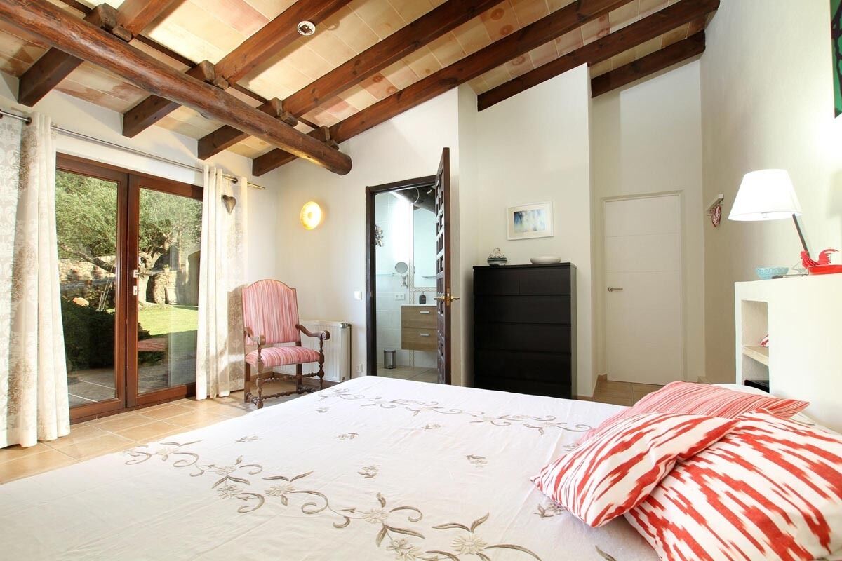 A bedroom with a bed, a chair, a wardrobe, and a door leading to a balcony.