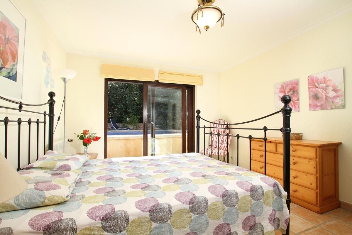 Een slaapkamer met een bed, een houten dressoir, een raam en een plafondlamp.